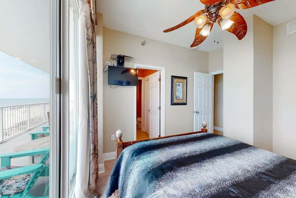 A bedroom with a bed beside sliding glass doors opening onto a balcony.