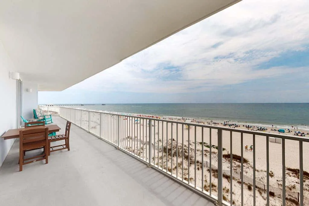 A balcony overlooking a sandy beach and the ocean, with outdoor seating.