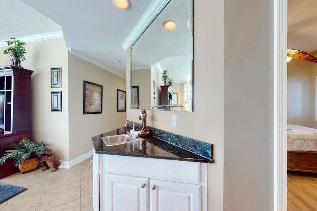 A bathroom vanity with a sink and mirror opens onto an adjacent bedroom.