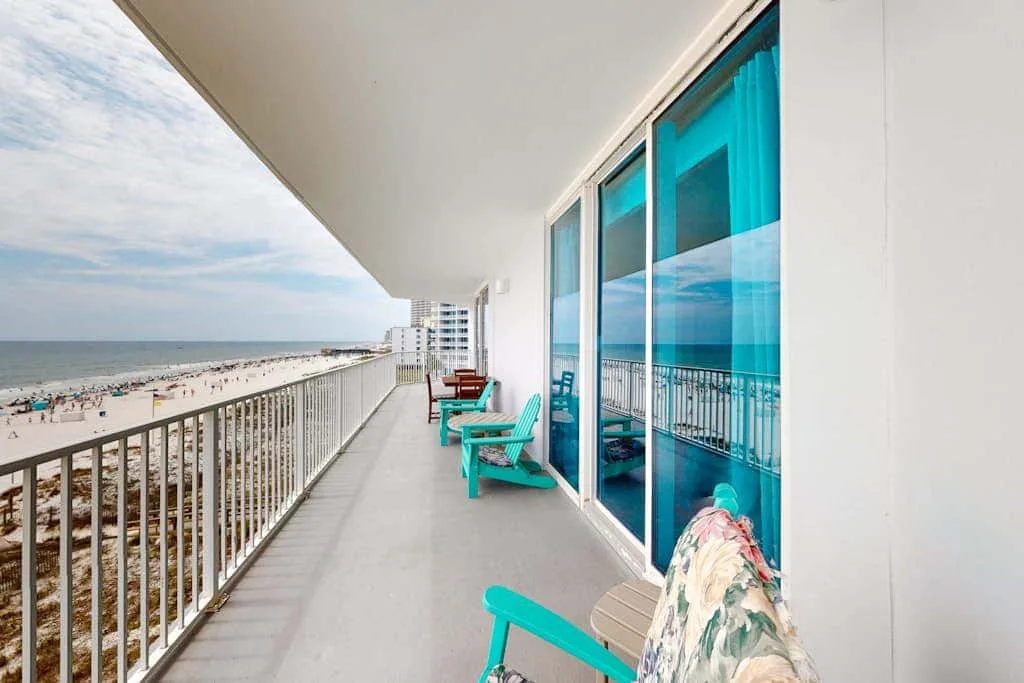 A balcony overlooks the beach and ocean, with turquoise seating beside glass doors.