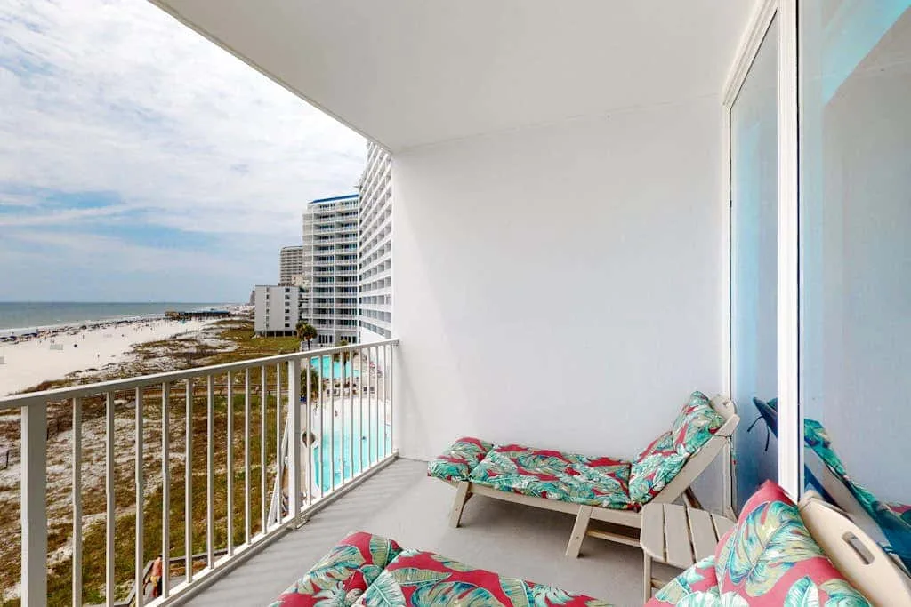 A balcony with colorful cushioned seating overlooks the beach and ocean.