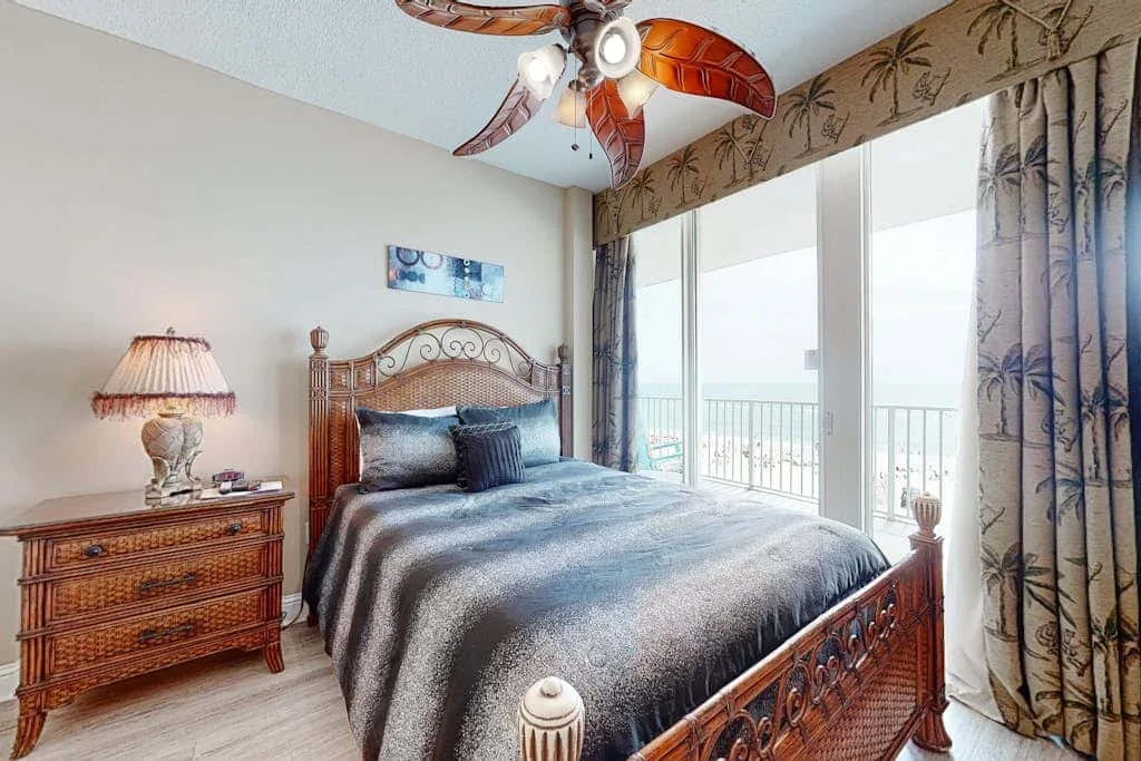 A bedroom with a neatly made bed beside large windows and curtains.