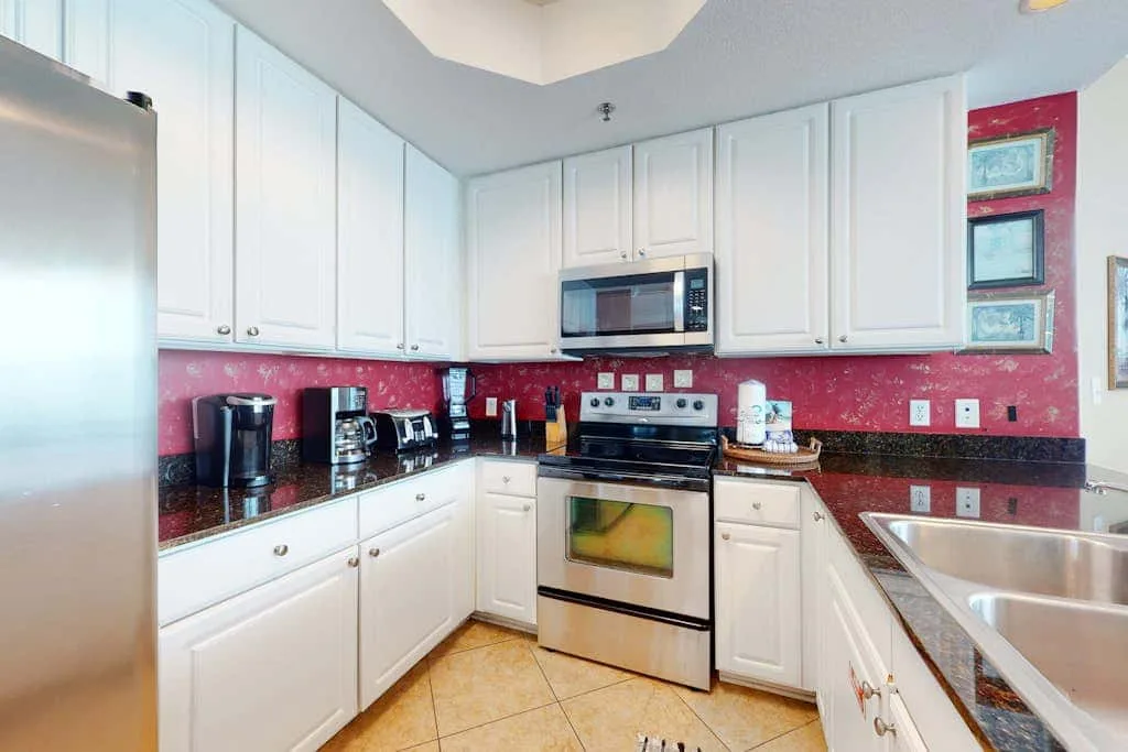 A bright kitchen with white cabinets, stainless steel appliances, and red patterned walls.
