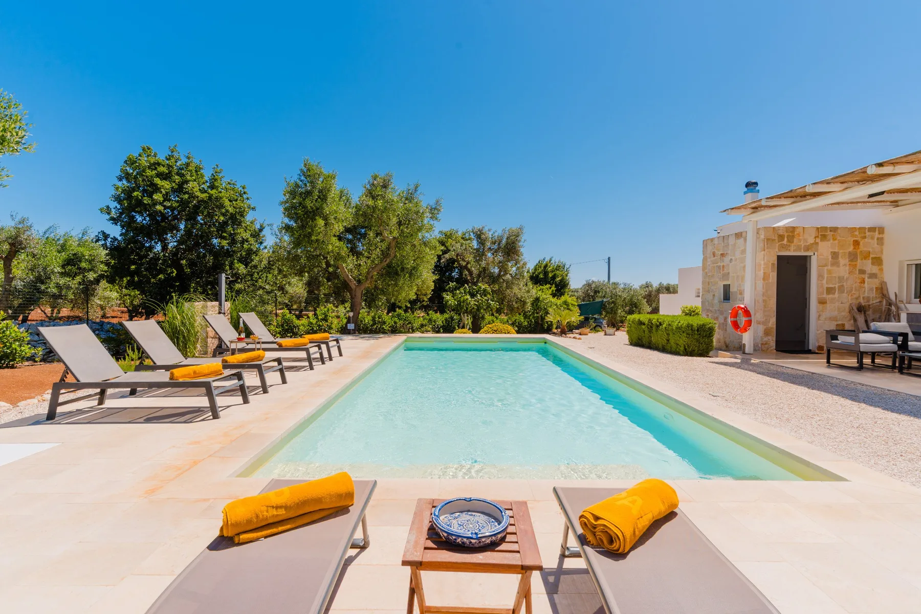 An outdoor swimming pool sits beside a stone building and rows of loungers.