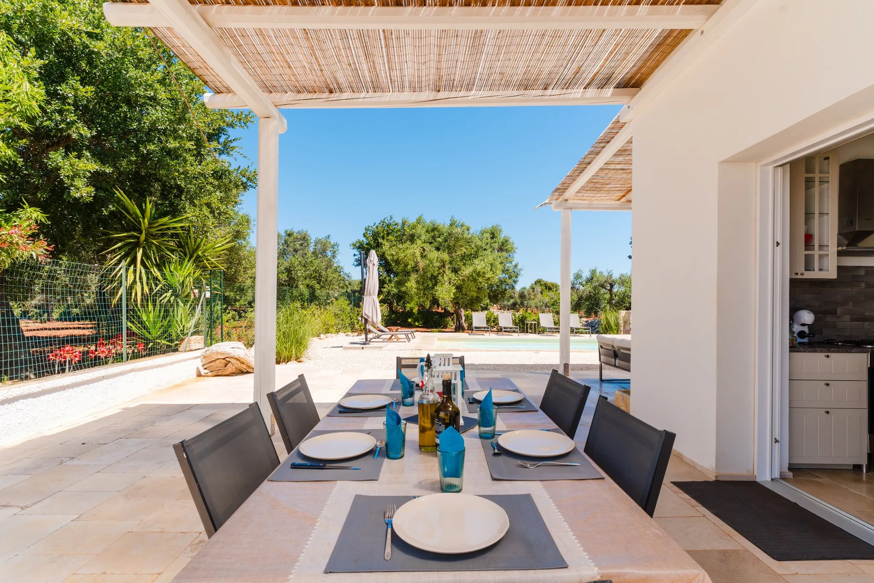 An outdoor dining area under a pergola overlooks a swimming pool and garden.