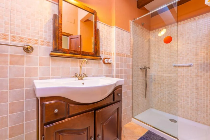 Un baño con azulejos, lavabo con mueble, espejo y ducha de cristal.