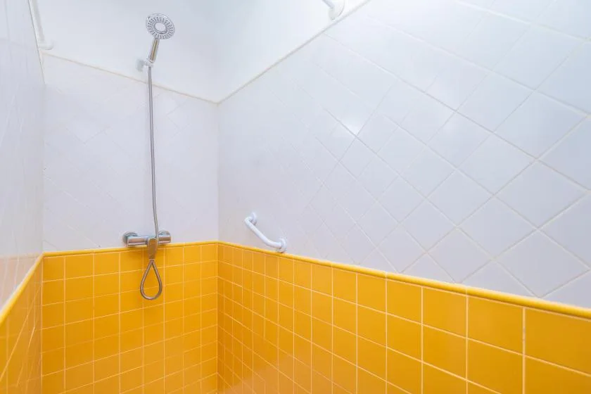 Una zona de ducha revestida con azulejos naranjas brillantes en la parte baja de las paredes.