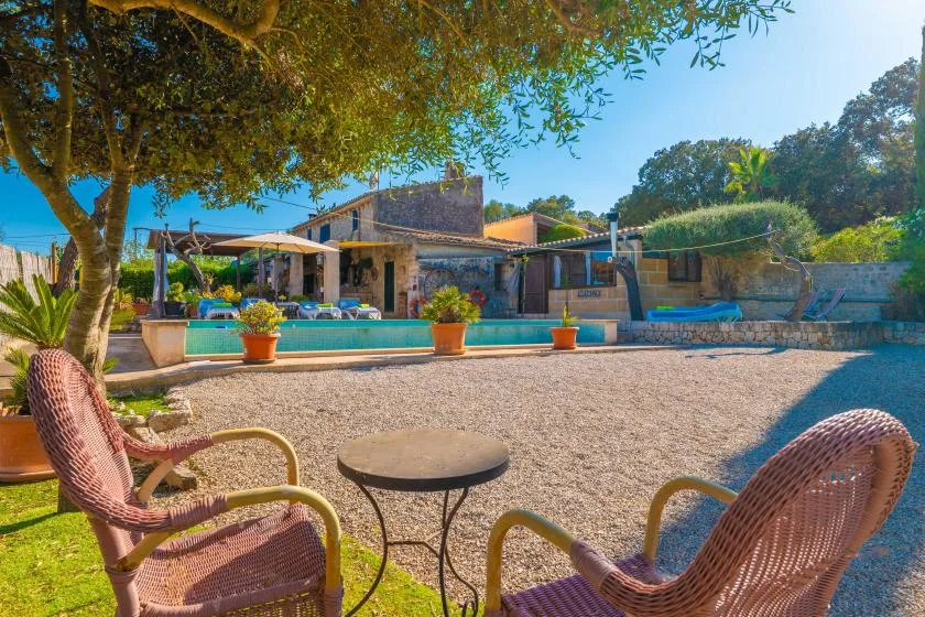 Un patio exterior da a una piscina y a un edificio bajo de piedra.
