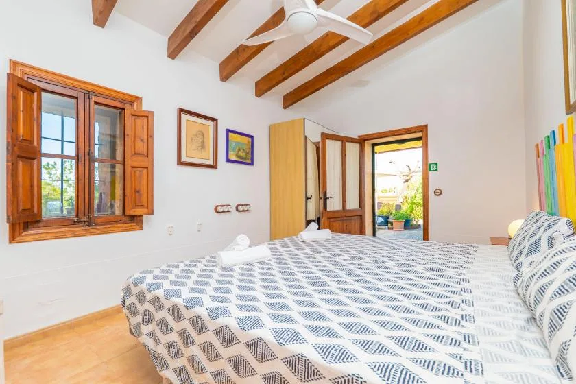 Un dormitorio con una cama estampada, vigas de madera en el techo y una puerta abierta.