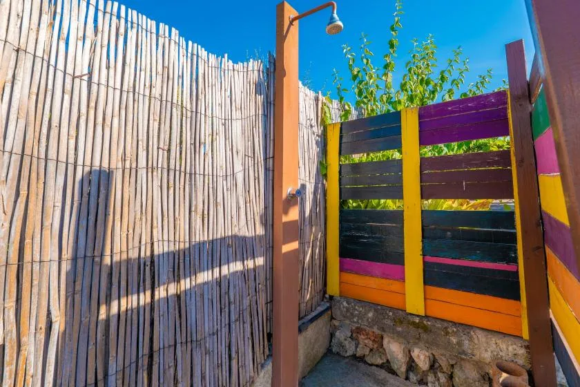Una zona de ducha exterior con una cerca de madera colorida y una pantalla de bambú.