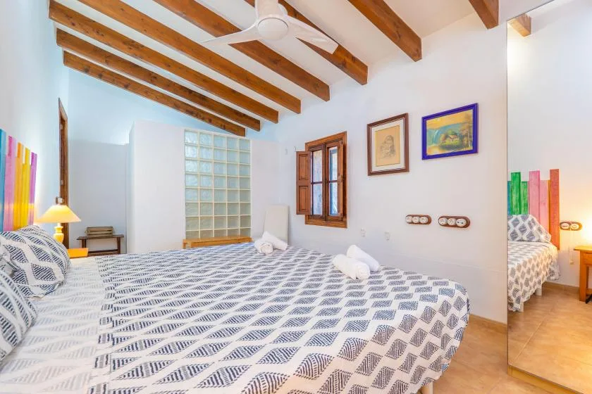Un dormitorio con ropa de cama estampada, vigas de madera vistas y una ventana.