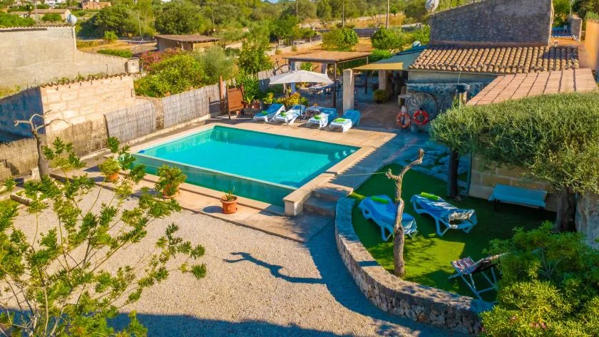 Una piscina al aire libre junto a un patio ajardinado con tumbonas y vegetación.