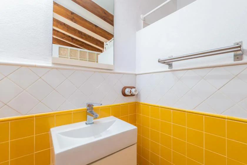 Un lavabo de baño está frente a paredes alicatadas de amarillo y blanco.