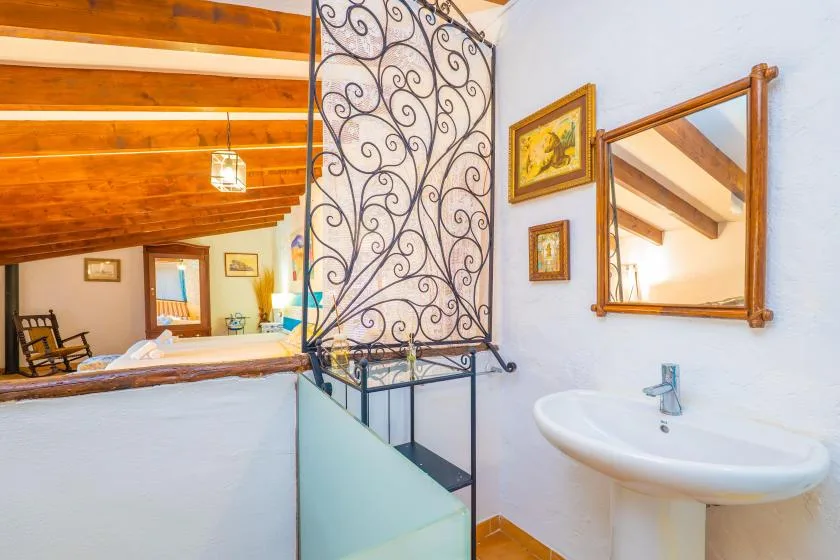 Un lavabo y un espejo dan a un dormitorio tipo loft bajo un techo de madera inclinado.