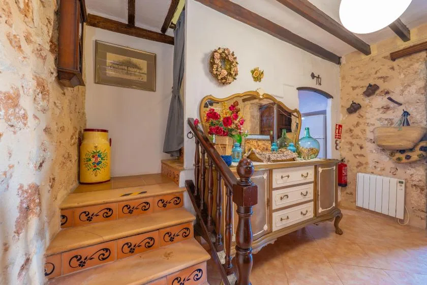 Un interior rústico con una escalera decorada junto a un aparador de madera y un espejo.