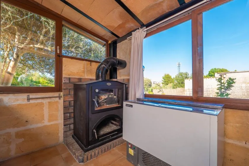 Una habitación iluminada por el sol con grandes ventanas, una estufa de leña y un congelador horizontal.
