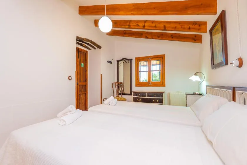 Un dormitorio luminoso con camas, vigas de madera y una ventana.