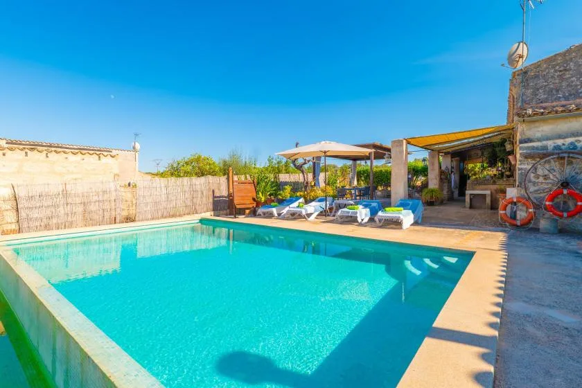 Una piscina al aire libre junto a un patio con asientos y una zona de sombra.
