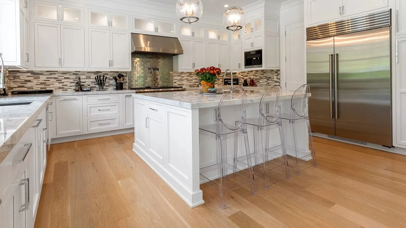 Una cocina luminosa con gabinetes blancos, una isla central y asientos transparentes.
