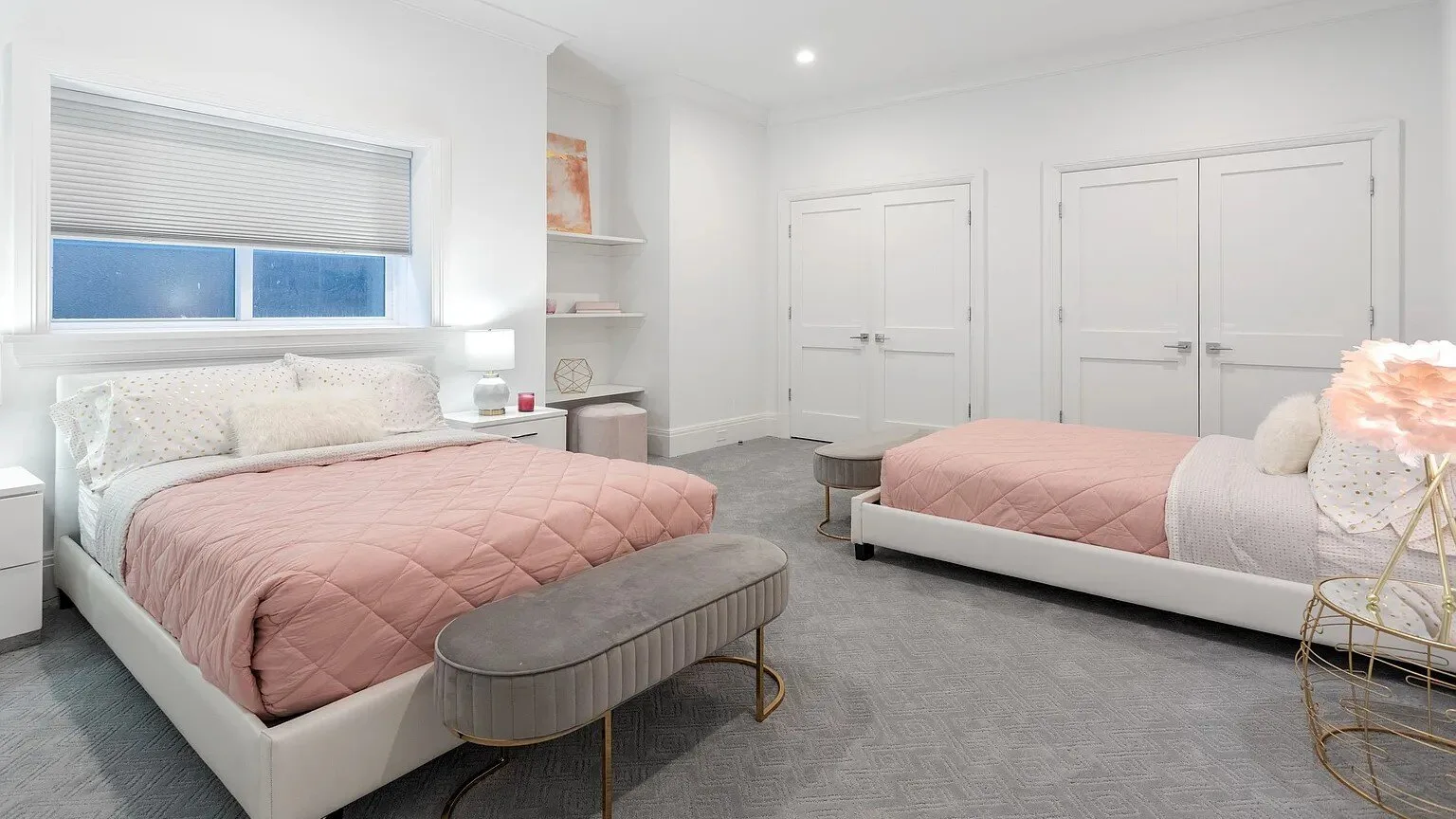 Un dormitorio luminoso con dos camas, alfombra gris y puertas blancas.