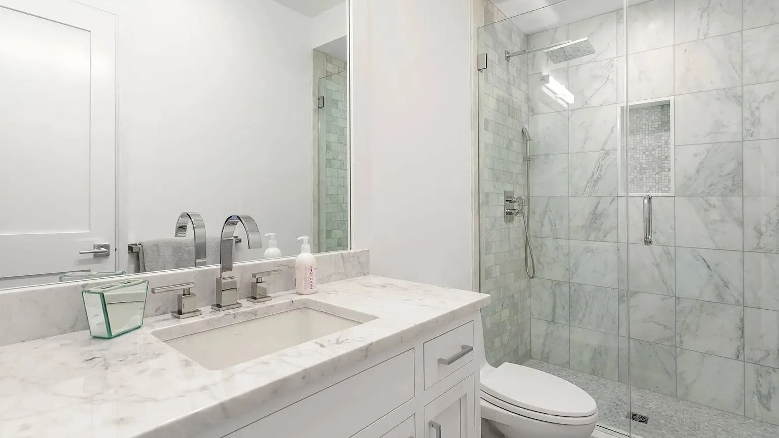 Un baño luminoso con tocador de mármol y ducha con mampara de vidrio.