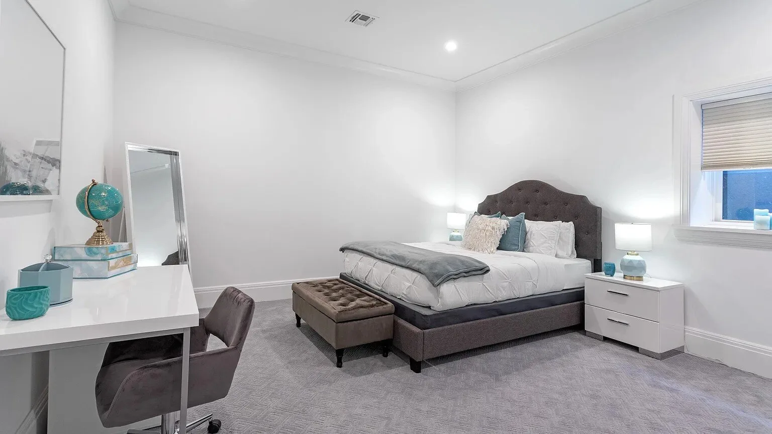 Un dormitorio luminoso con una cama, mesitas de noche y un escritorio junto a la pared.