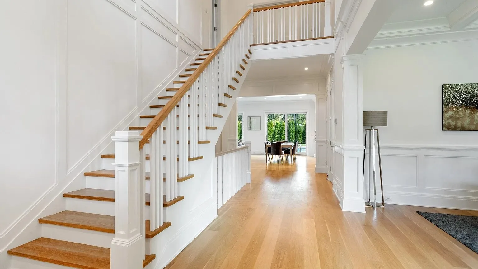 Un pasillo luminoso con una escalera de madera y un comedor abierto al fondo.