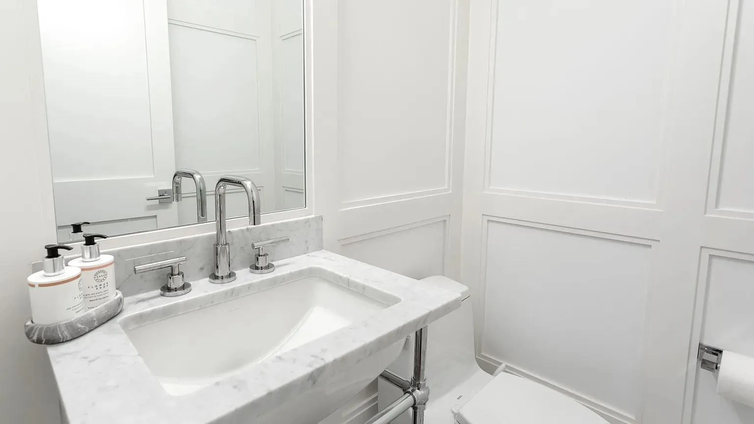 Un baño luminoso con lavabo blanco, grifos cromados y paredes con paneles.