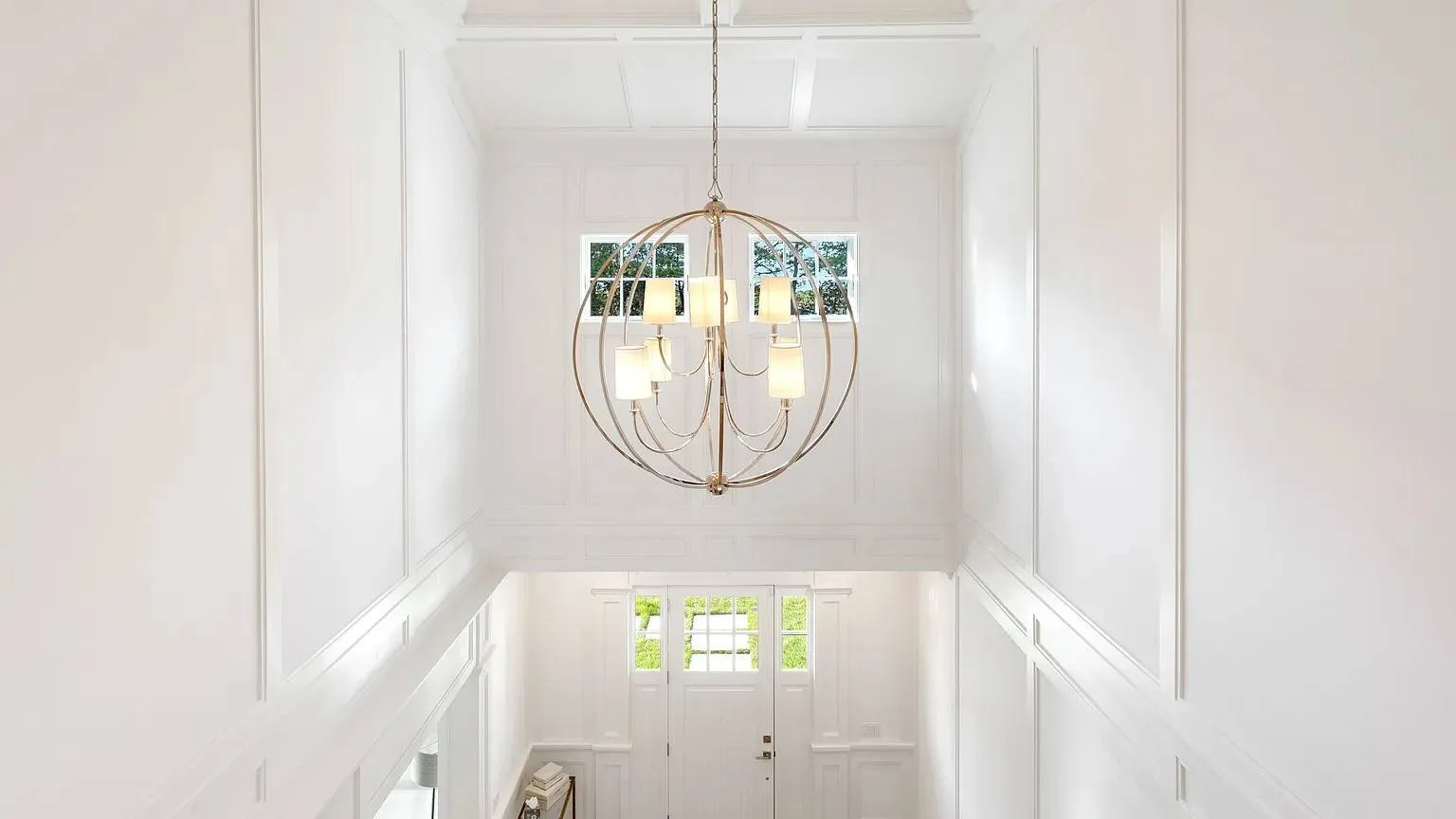 Una entrada blanca y luminosa con una puerta principal y una lámpara colgante.