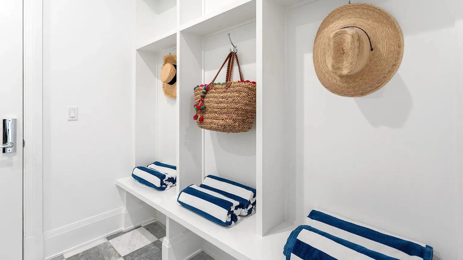 Una entrada luminosa con compartimentos empotrados, cojines a rayas y sombreros y bolsos tejidos.