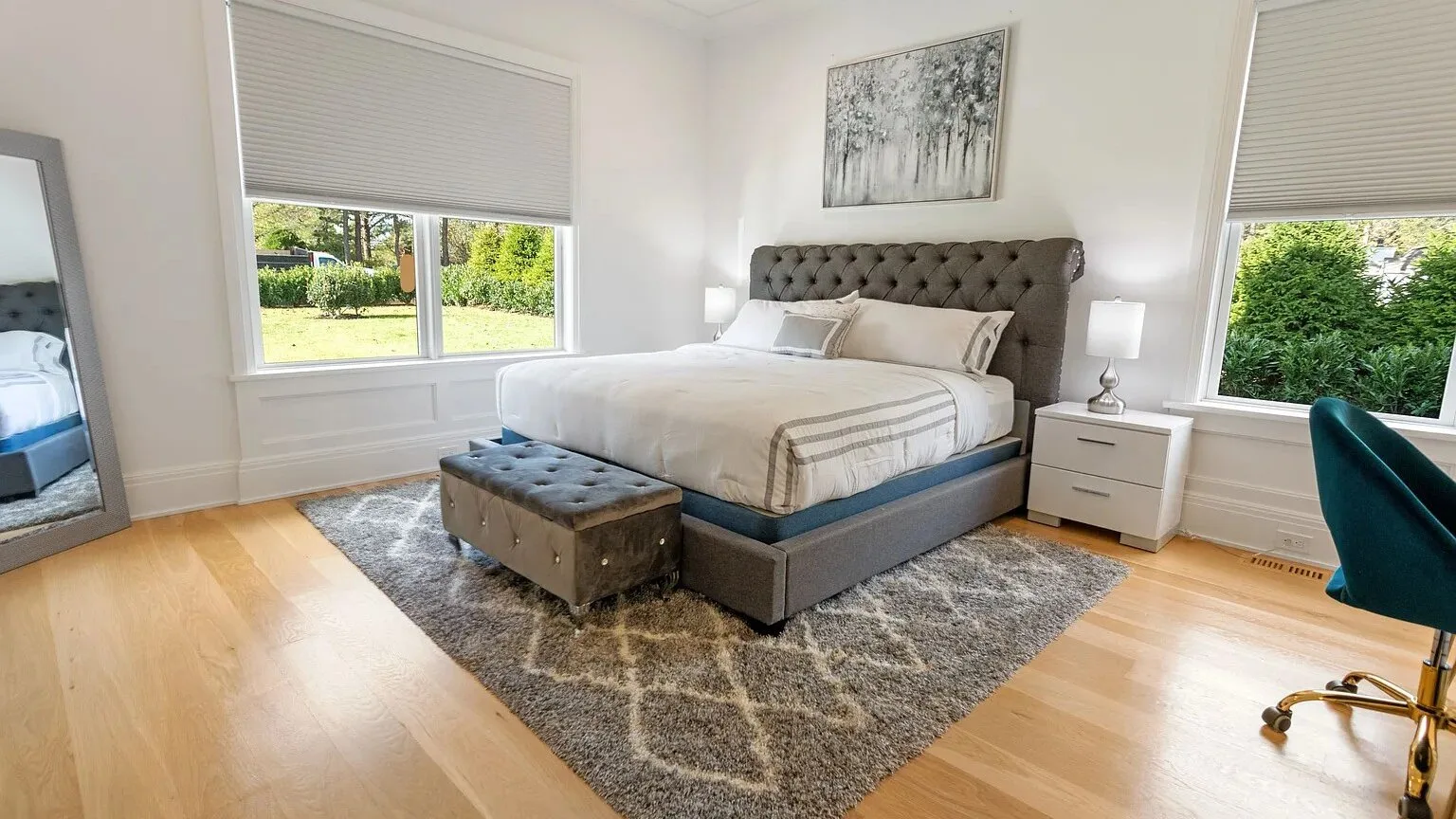 Un dormitorio luminoso con una cama, mesitas de noche y grandes ventanas.