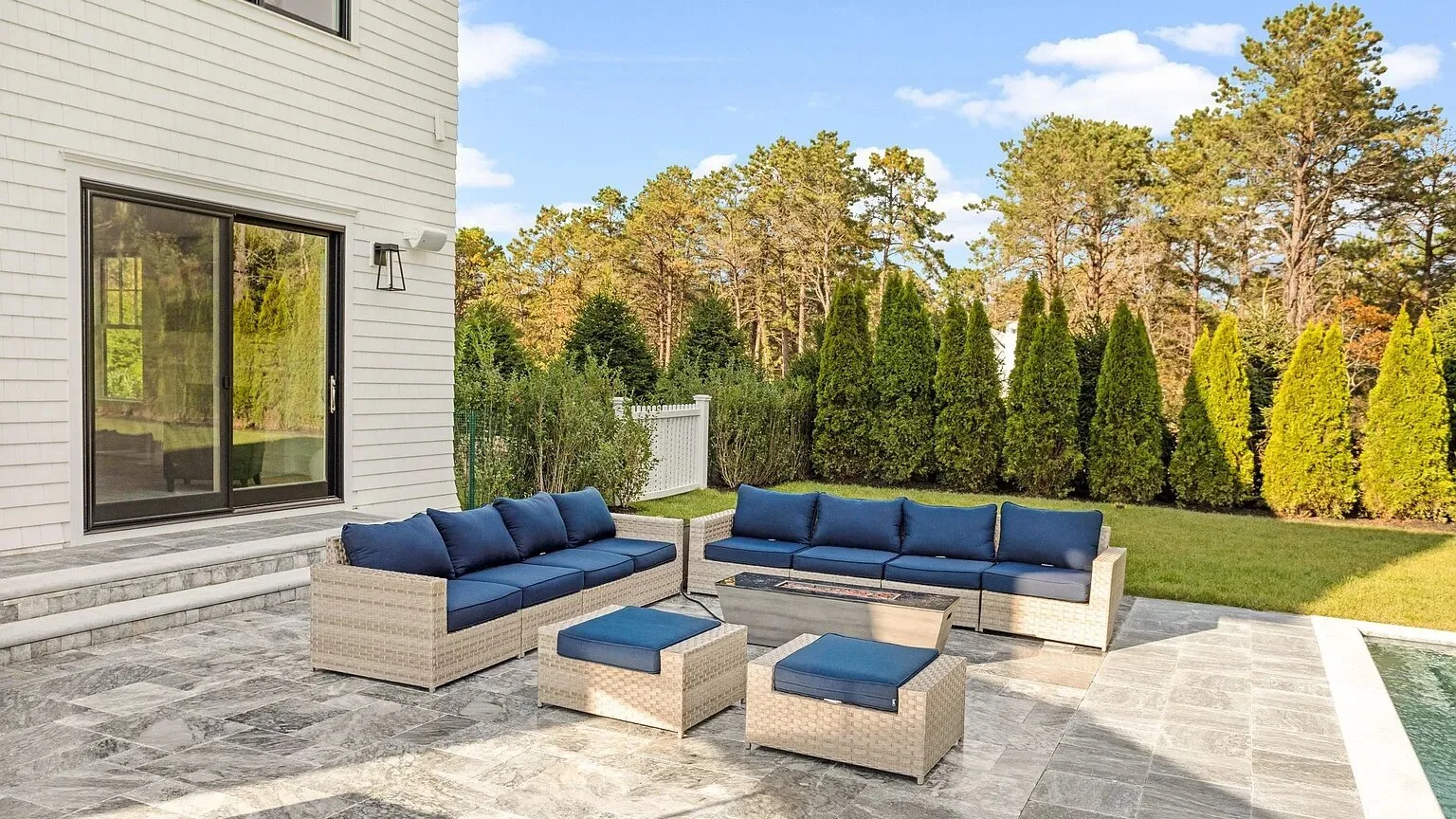Un patio pavimentado tiene asientos con cojines azules junto a la casa.