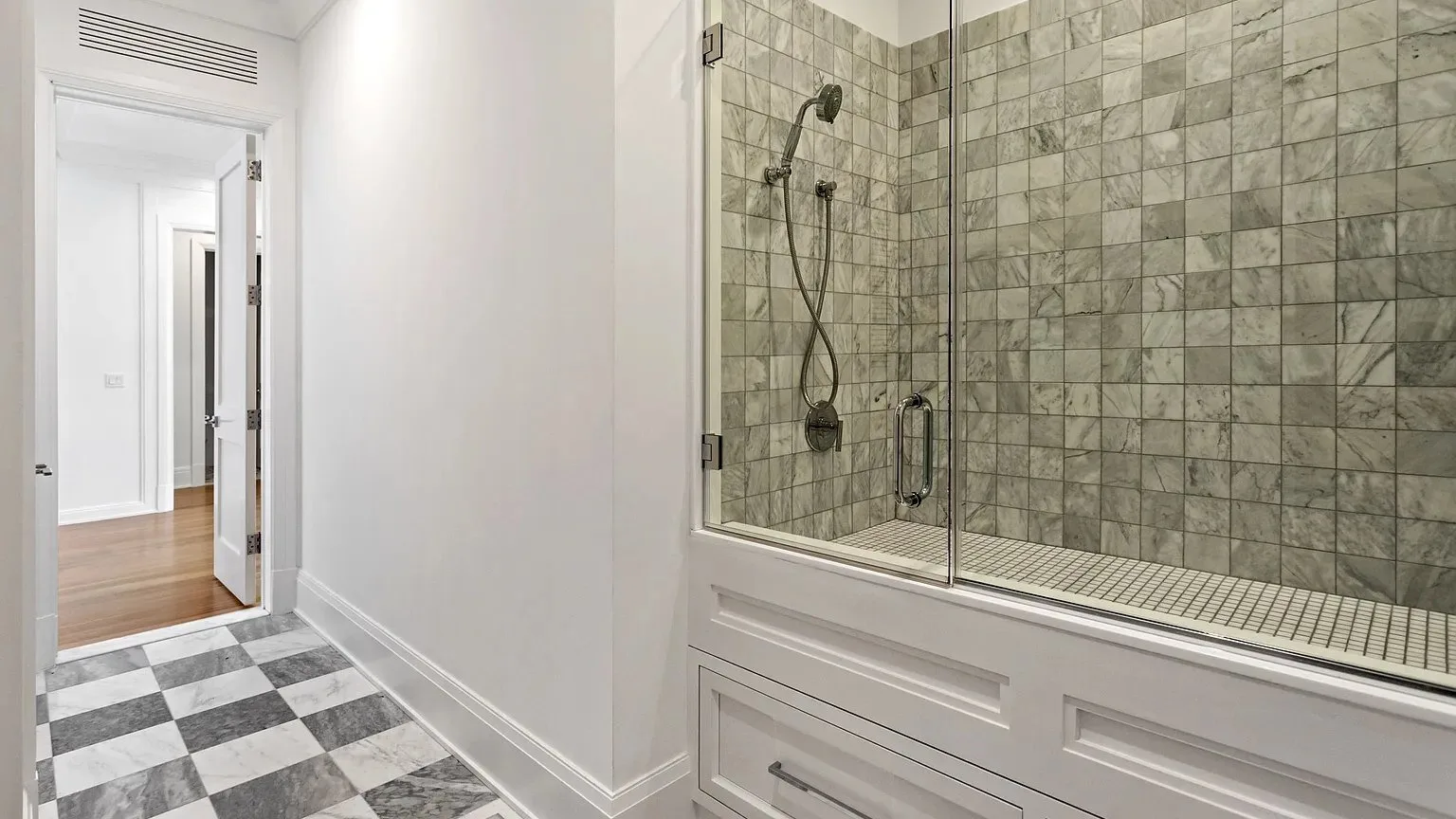 Un baño con una ducha revestida de azulejos detrás de una mampara de vidrio.