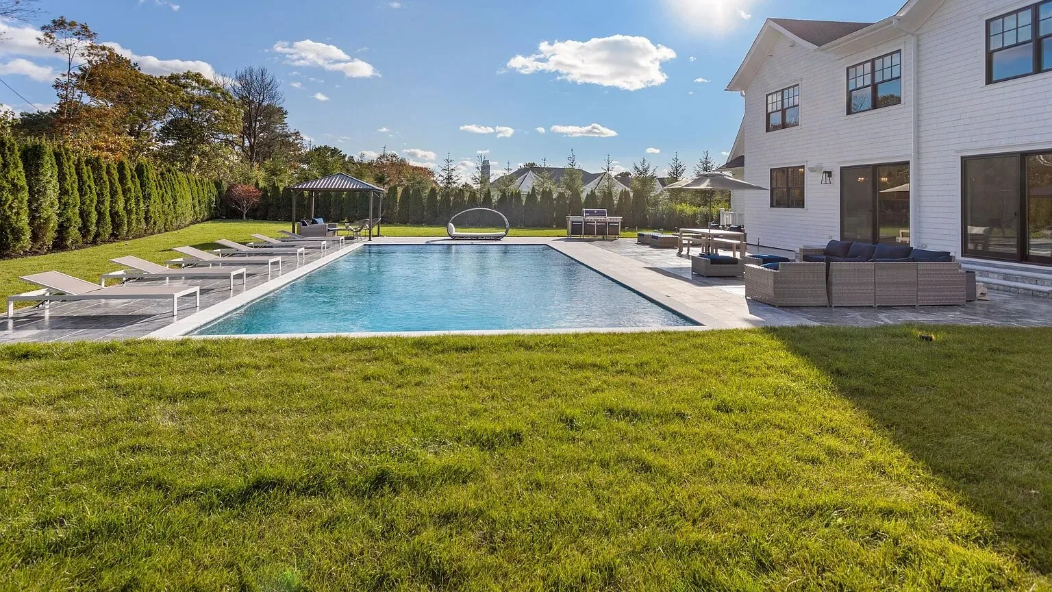 Piscina al aire libre junto a una casa, con césped y asientos de descanso.