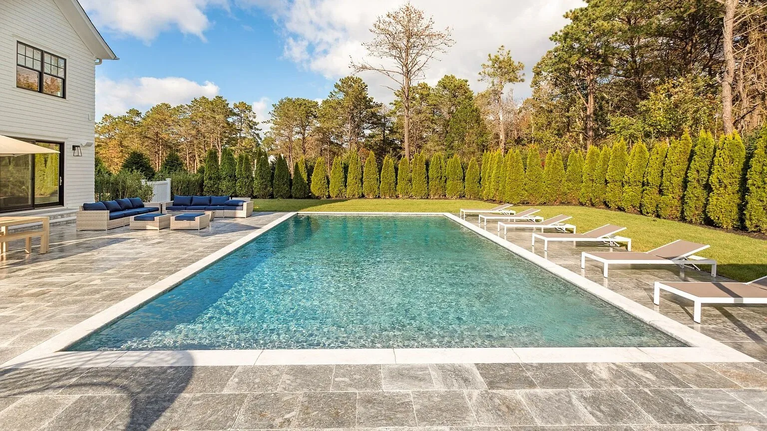 Una piscina al aire libre junto a un patio pavimentado y varias tumbonas.