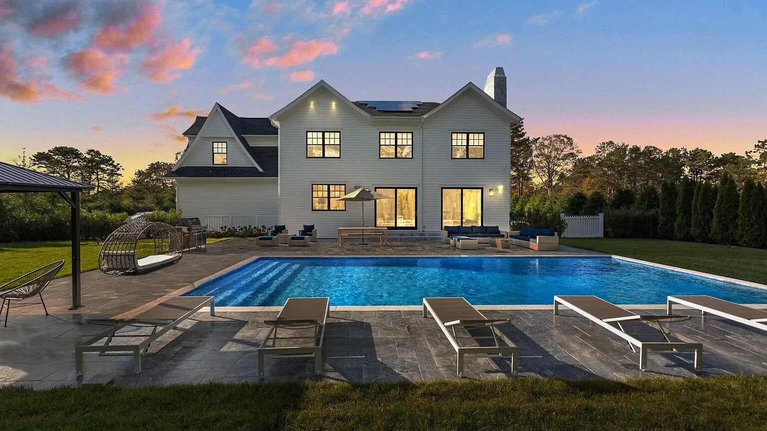 Una casa y una piscina al atardecer, con asientos alrededor de la piscina.
