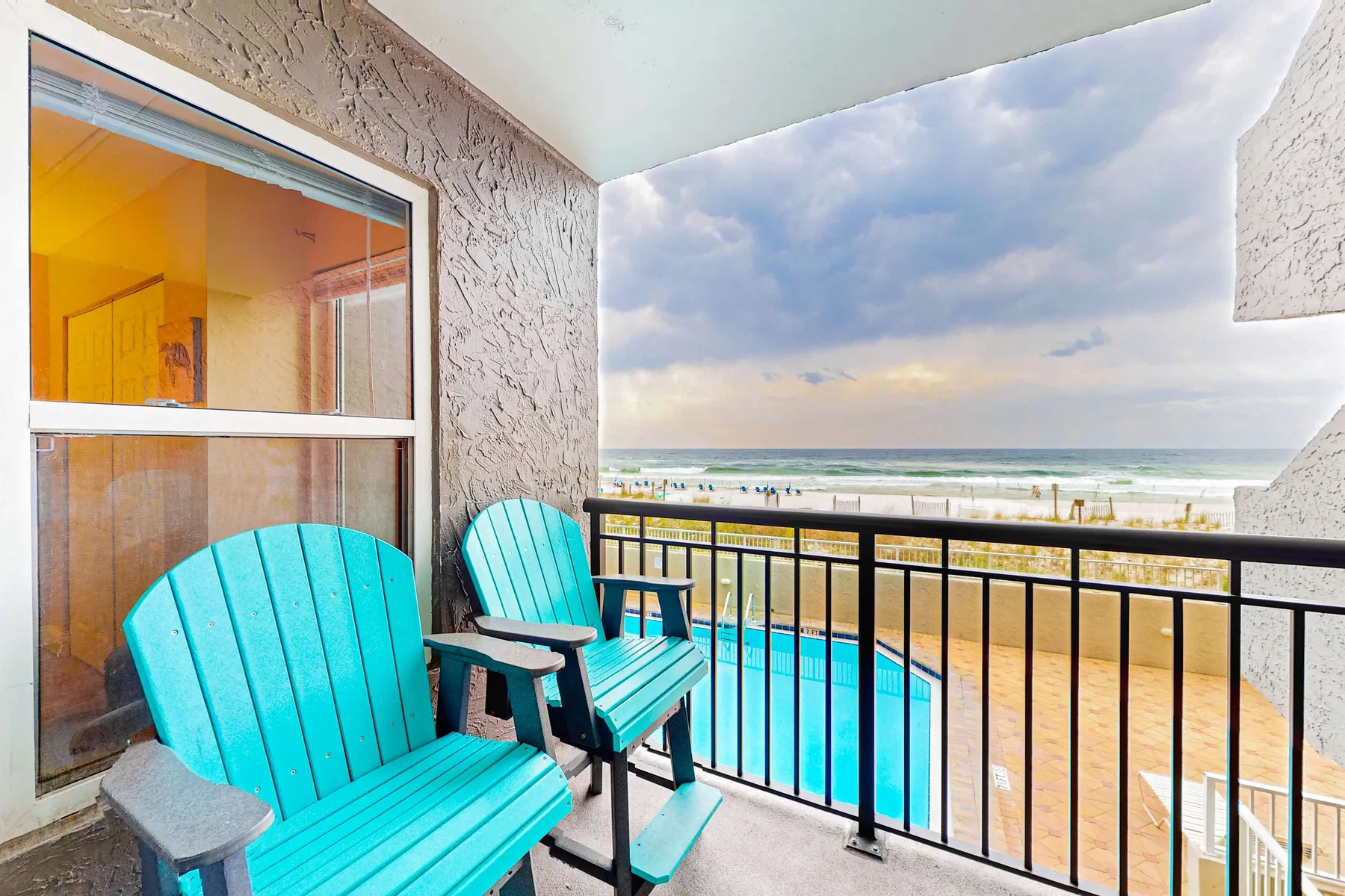 A balcony with turquoise seating overlooks a sandy beach and ocean.