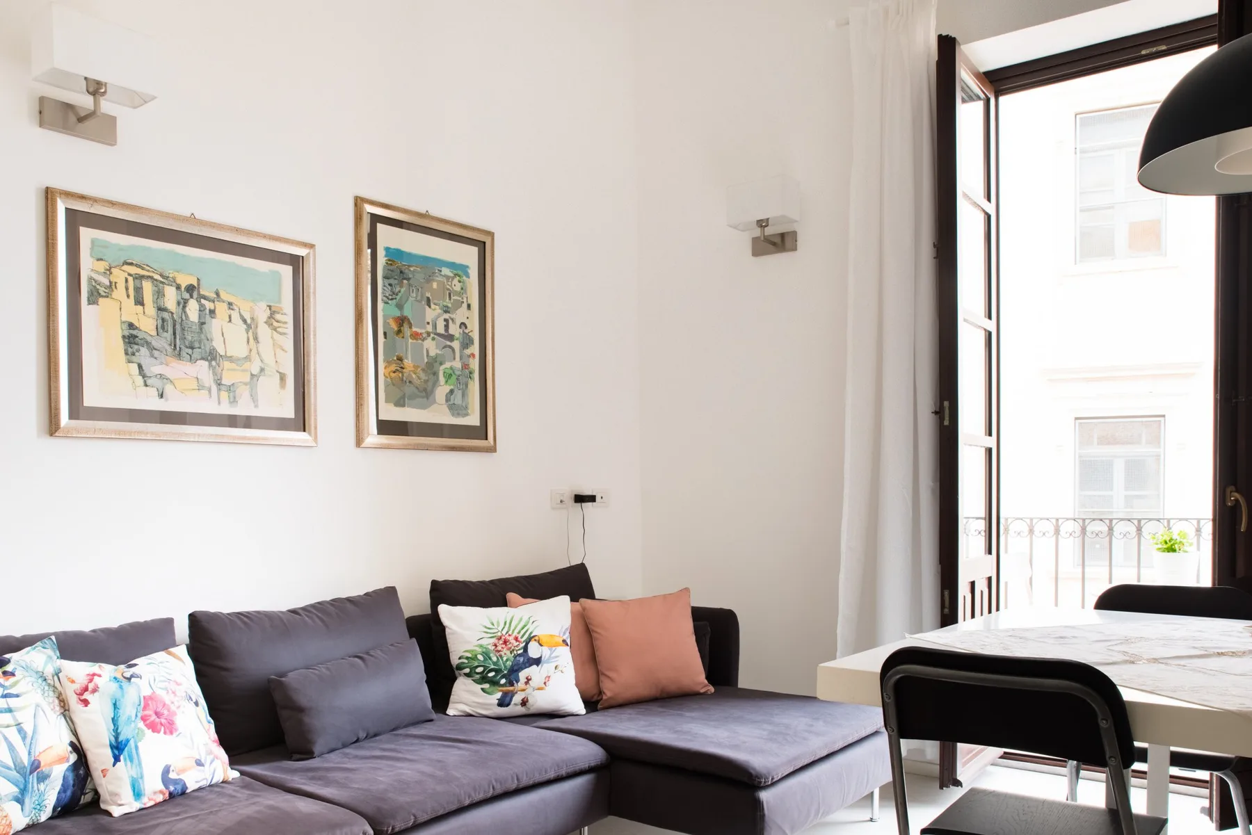 Una sala de estar con un sofá seccional, cuadros enmarcados y una ventana abierta.