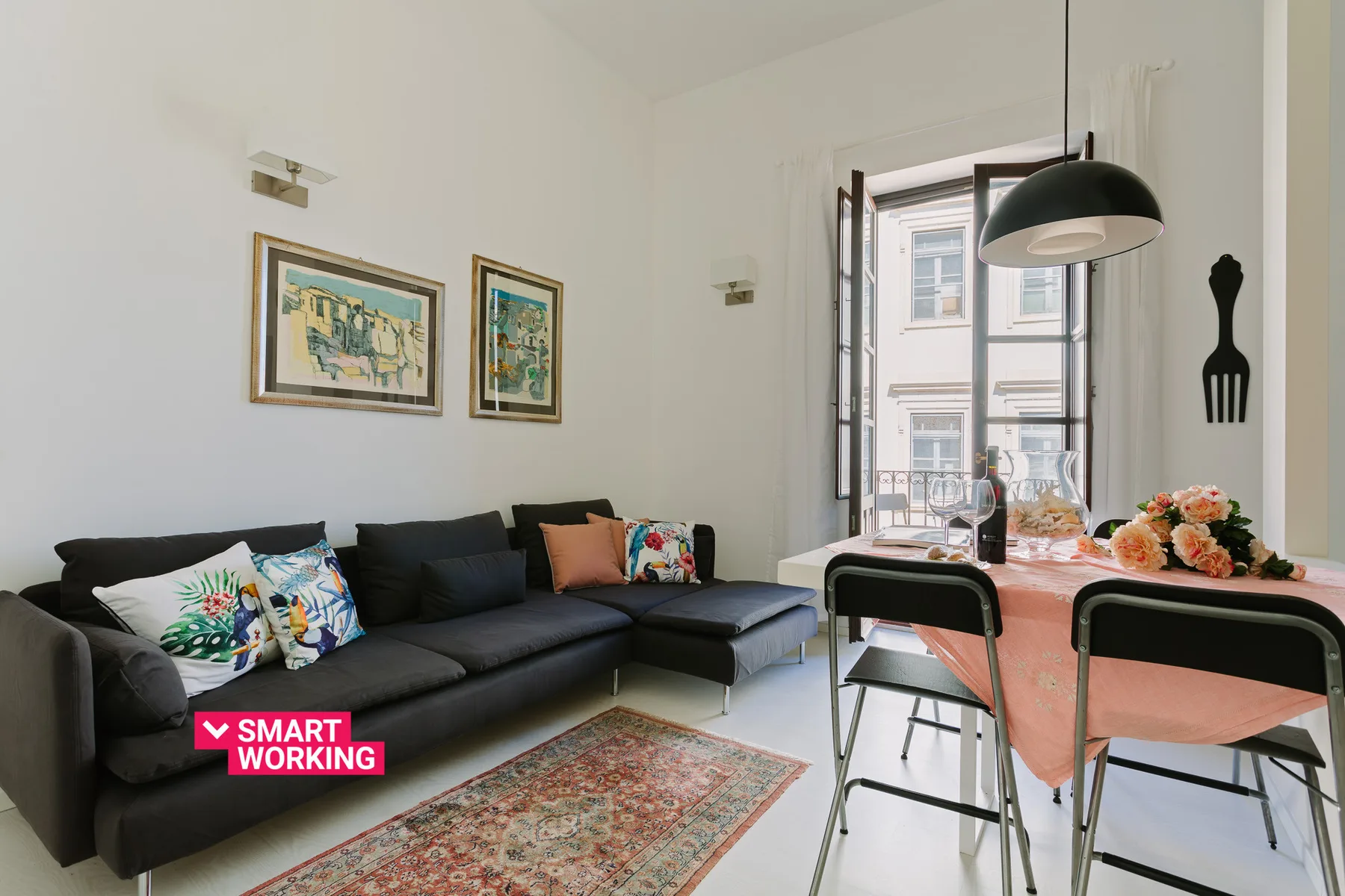 Una sala y comedor con un sofá seccional oscuro y una mesa junto a la ventana.