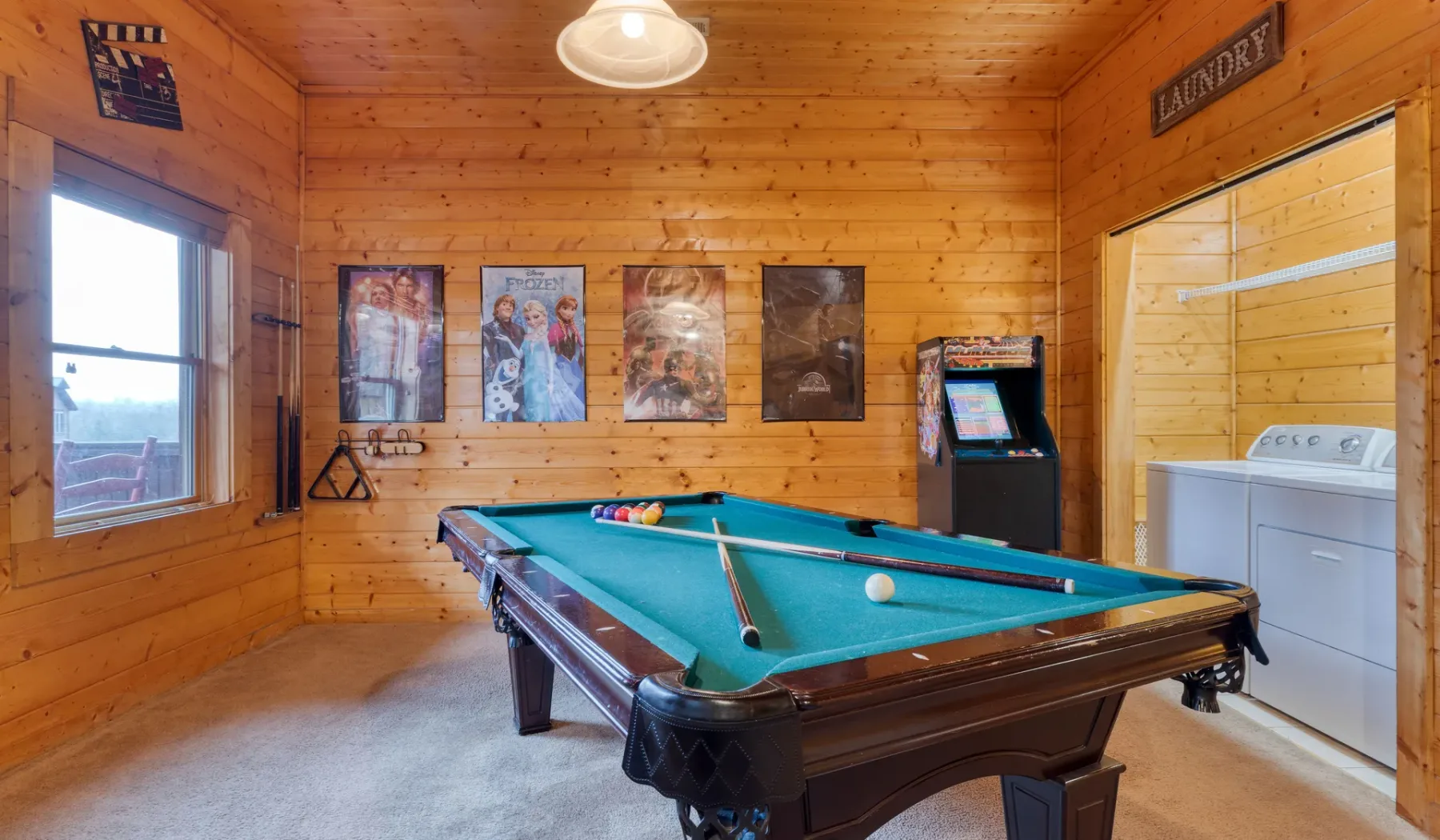 Una sala de juegos revestida de madera con una mesa de billar y una máquina recreativa.