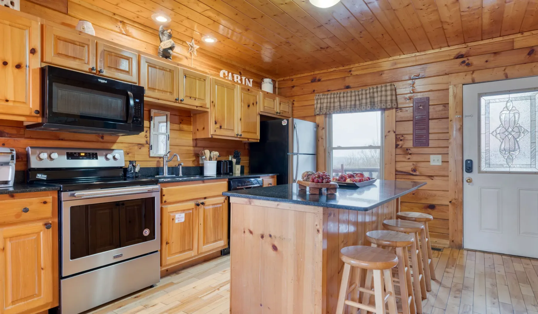Una cocina revestida de madera con isla, asientos junto a la barra y electrodomésticos de acero inoxidable.