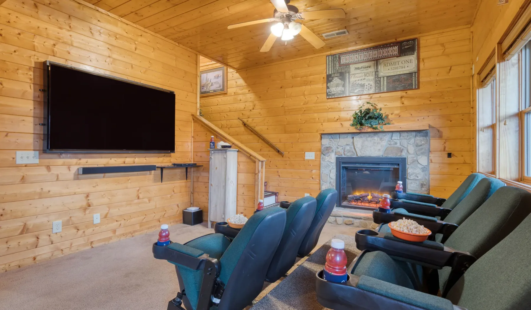 Una sala de entretenimiento revestida de madera tiene asientos reclinables frente a un televisor y una chimenea.