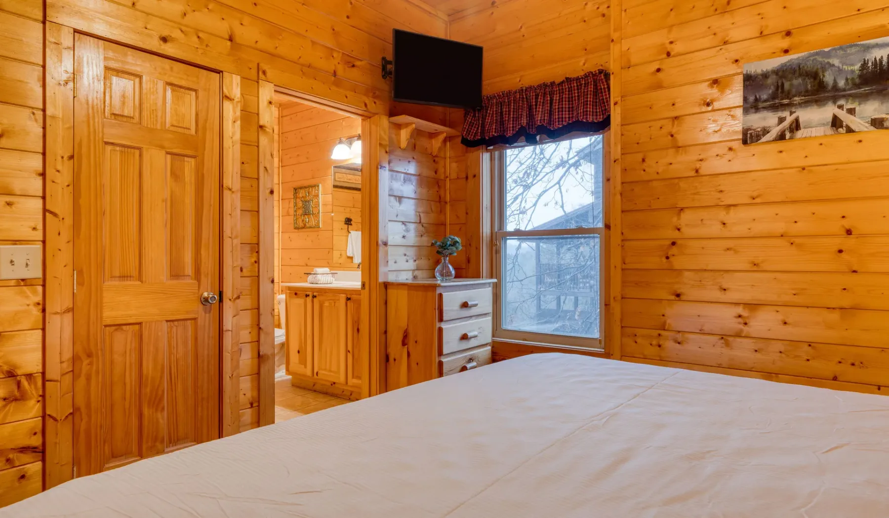 Un dormitorio revestido de madera con una cama, una cómoda y una ventana.