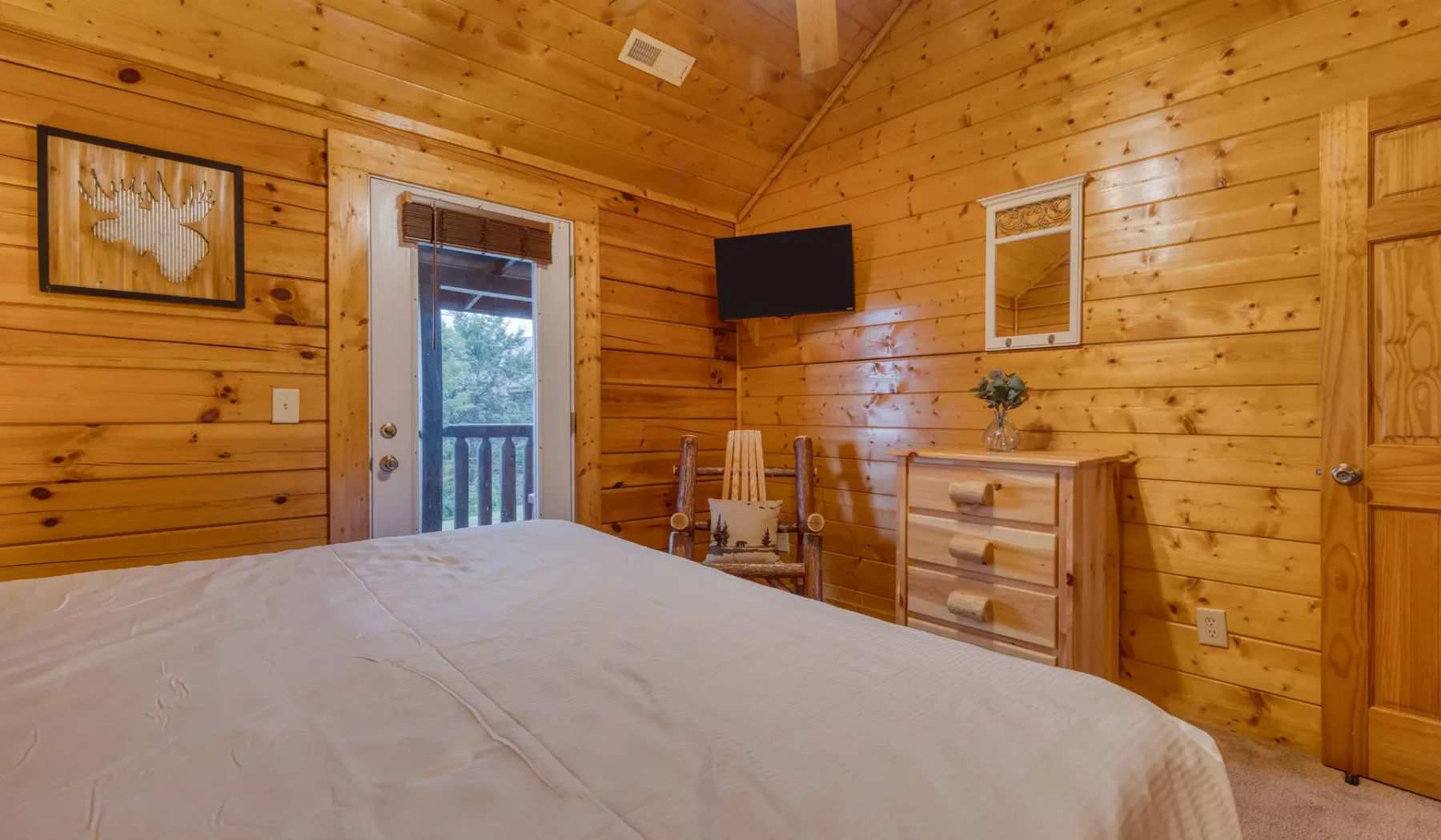 Dormitorio con paredes de madera, una cama y un televisor montado en la pared.