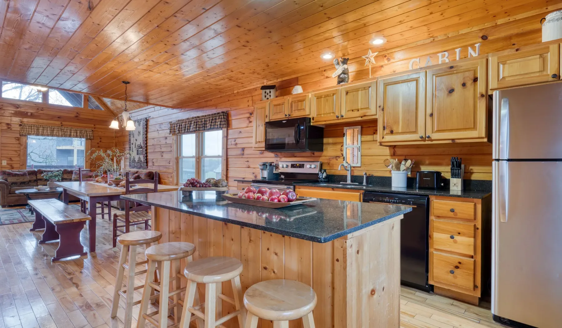 Una cocina revestida de madera, con una isla central y taburetes, se abre a un comedor.