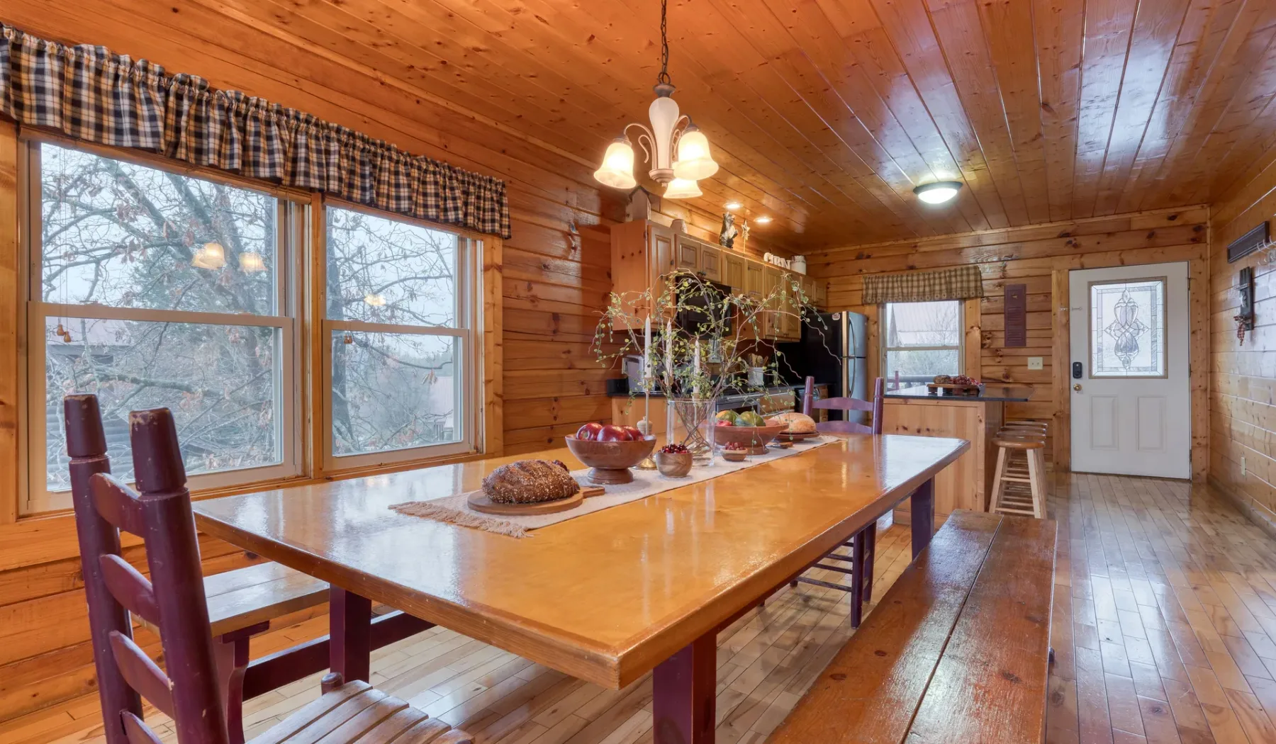 Comedor revestido de madera con una mesa larga junto a grandes ventanas.