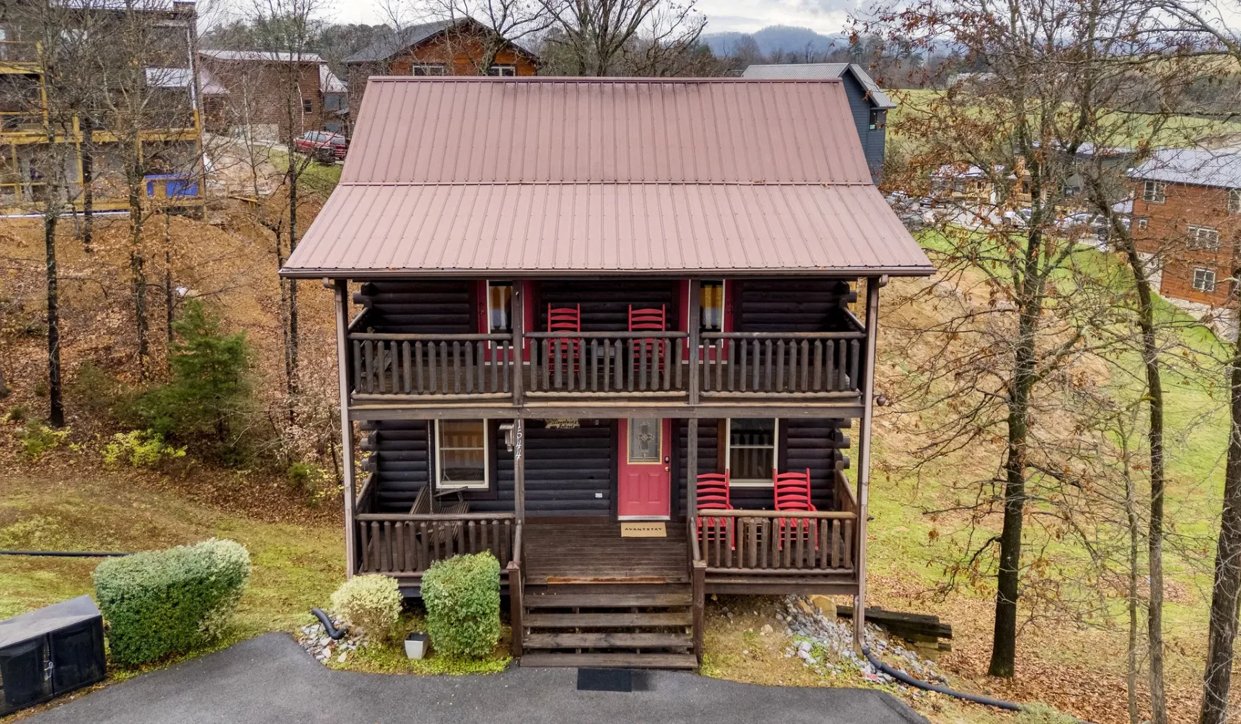 Una cabaña de madera oscura con dos balcones cubiertos y sillas rojas.