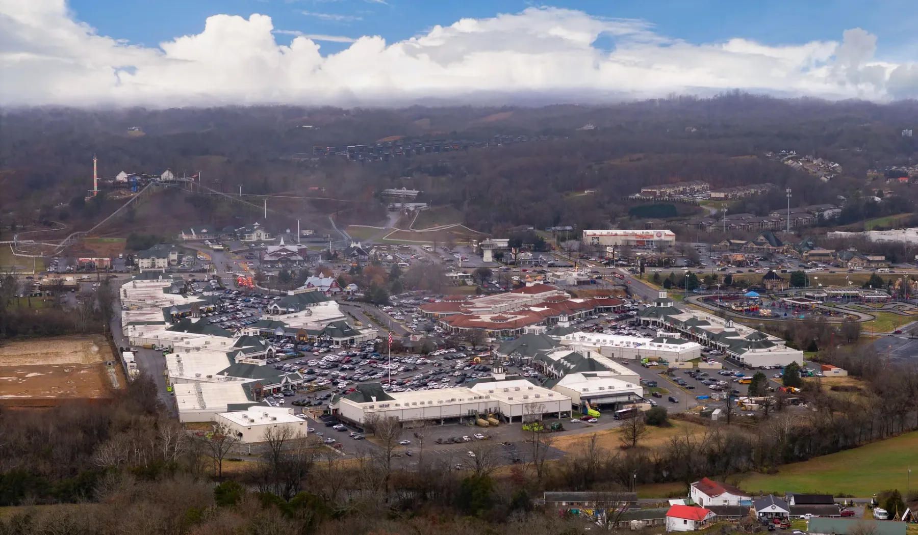 Vista aérea de una zona comercial con colinas boscosas al fondo.