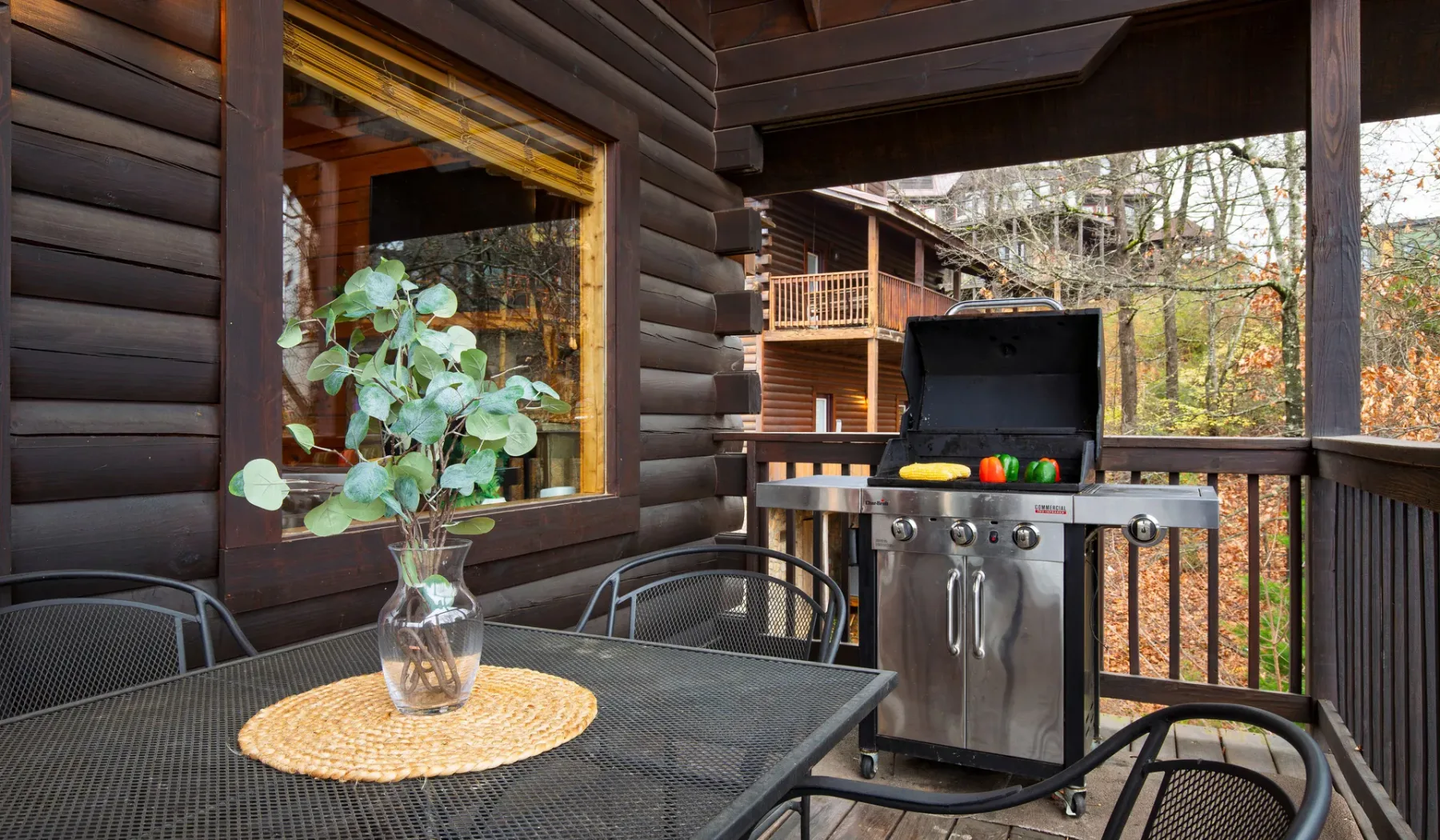Una terraza cubierta de madera con una mesa de comedor metálica y una parrilla abierta.
