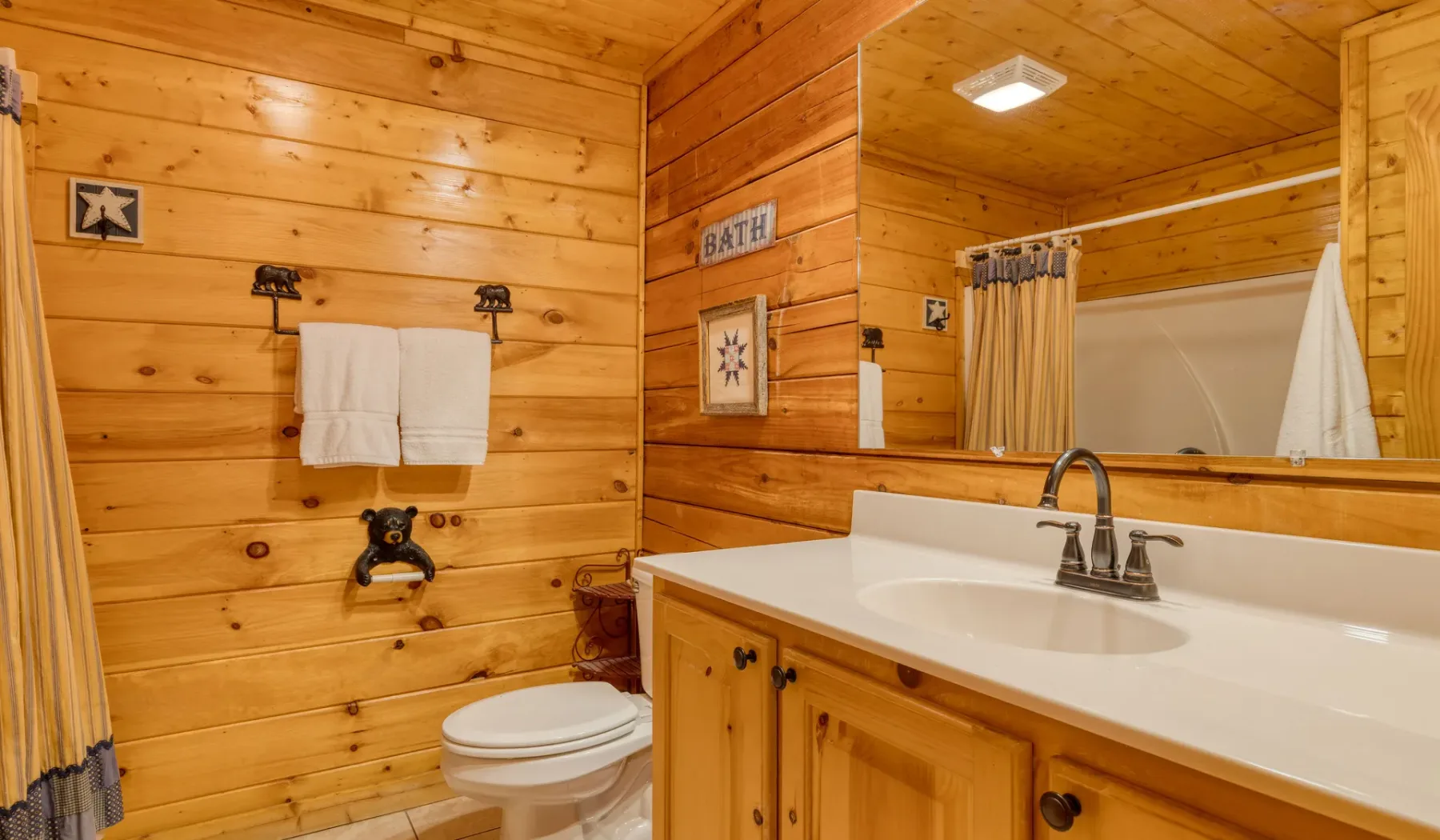 Un baño revestido de madera con lavabo, espejo e inodoro.